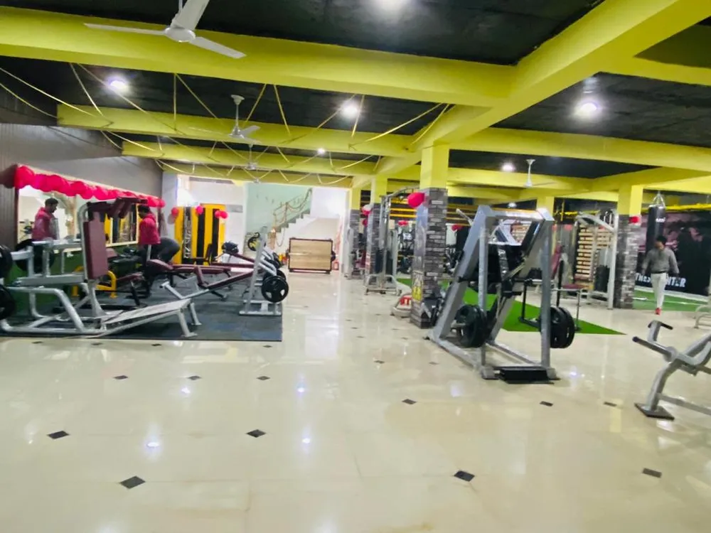 A wide view of the gym floor: a bench and free-weight rack in the foreground, rows of exercise machines beyond it, and a punching bag hanging in the far corner, under a ceiling of exposed beams and multiple ceiling fans.